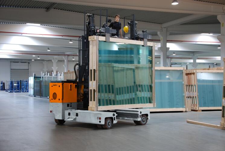 HUBTEX Mehrwege-Seitenstapler beim Transport von Glasgestellen in der Lagerhalle