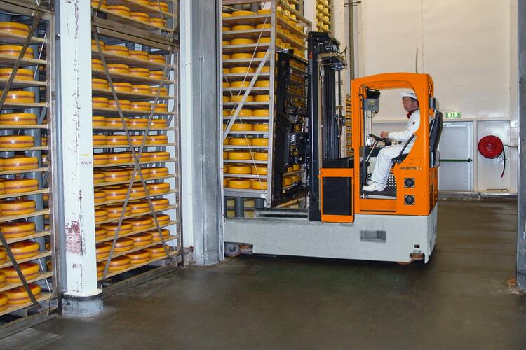 The reach truck drives under the rack of cheese wheels and picks it up on the forks