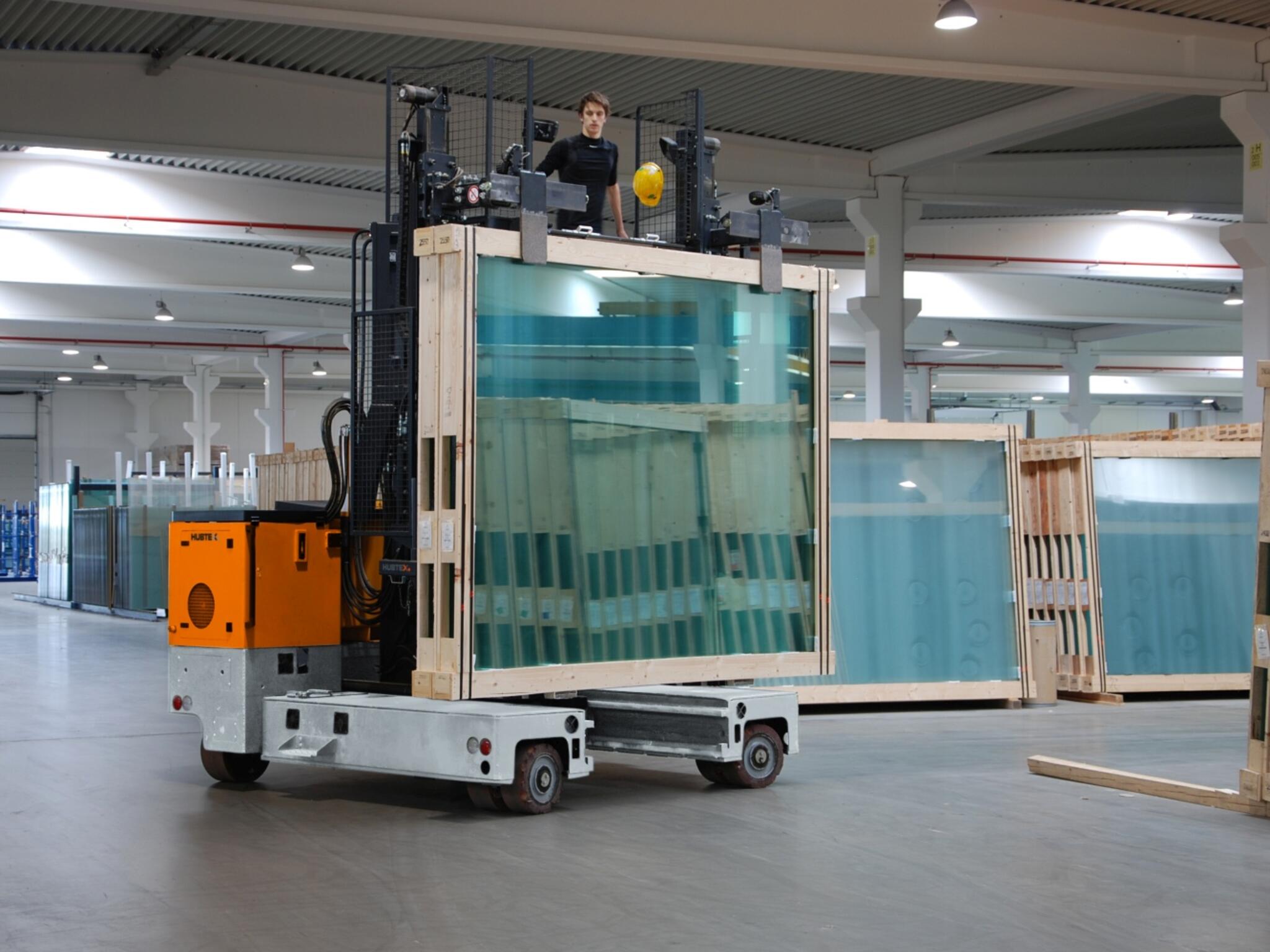 HUBTEX Mehrwege-Seitenstapler beim Transport von Glasgestellen in der Lagerhalle