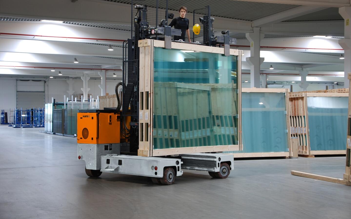 Carretilla elevadora multidireccional de carga lateral HUBTEX durante el transporte de bastidores de vidrio en una nave industrial